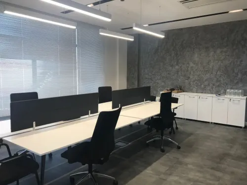 Karşılıklı masa düzeni, siyah ara paneller ve beyaz depolama üniteleriyle açık ofis alanı, ekip çalışması için kontrollü ve işlevsel bir yapı sunar.