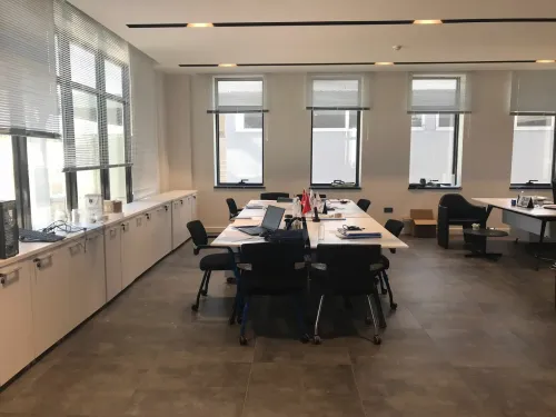 Geniş pencere önü, çalışma masaları, siyah ofis koltukları ve depolama üniteleriyle kurgulanan alan, kurumsal ofis kullanımına düzenli bir yapı kazandırır.