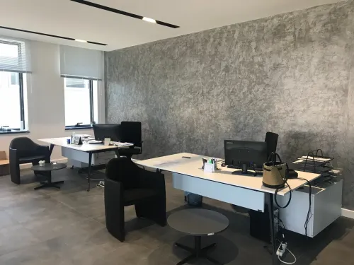 Gri duvar dokusu, beyaz masa yüzeyleri ve siyah ofis koltuklarıyla oluşturulan çalışma alanı, modern ofis projesine sakin bir kurumsal karakter verir.