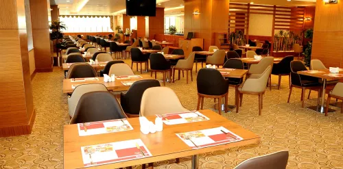 Ahşap masa yerleşimi, açık ve koyu tonlu sandalyelerle düzenlenen restoran alanı, otel misafirleri için sıcak ve dengeli bir atmosfer sunar.
