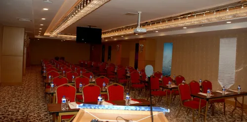 Sunum ekipmanı, kırmızı sandalye sıraları ve geniş salon perspektifiyle konferans alanı, organizasyonlara uygun işlevsel bir düzen sunar.
