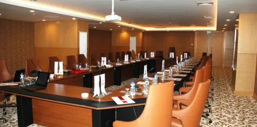 Uzun toplantı masası, turuncu sandalyeler ve teknik sunum düzeniyle toplantı salonu, kurumsal otel etkinlikleri için işlevsel bir alan oluşturur.