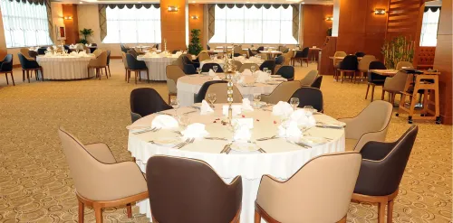 Yuvarlak masa yerleşimi, açık renkli sandalyeler ve sıcak iç mekân diliyle restoran alanı, otel kullanımı için davetkâr bir düzen sunar.