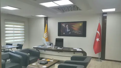 Yönetici masası, Türk bayrağı, kurum bayrağı ve oturma alanıyla düzenlenen ofis, üniversite yönetimi için resmi ve kurumsal bir mekân dili sunar.